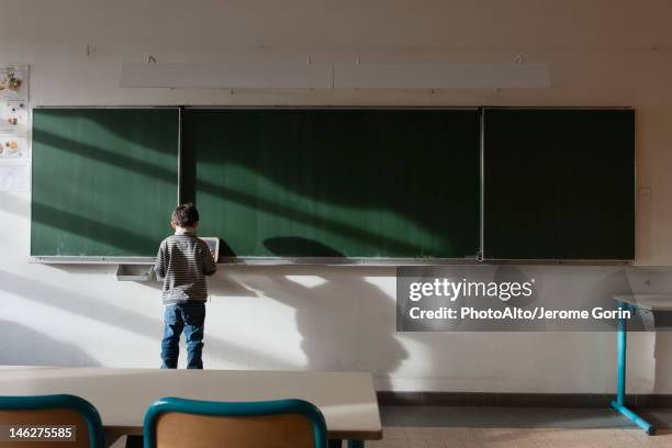 boy standing in classroom, in front of blackboard, rear view - schoolboy stock pictures, royalty-free photos & images