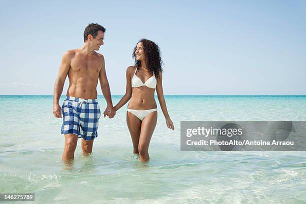 couple wading hand in hand at the beach - couple swimwear stock pictures, royalty-free photos & images