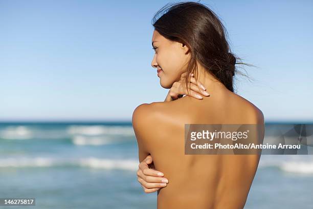 naked young woman looking at ocean, rear view - nua imagens e fotografias de stock