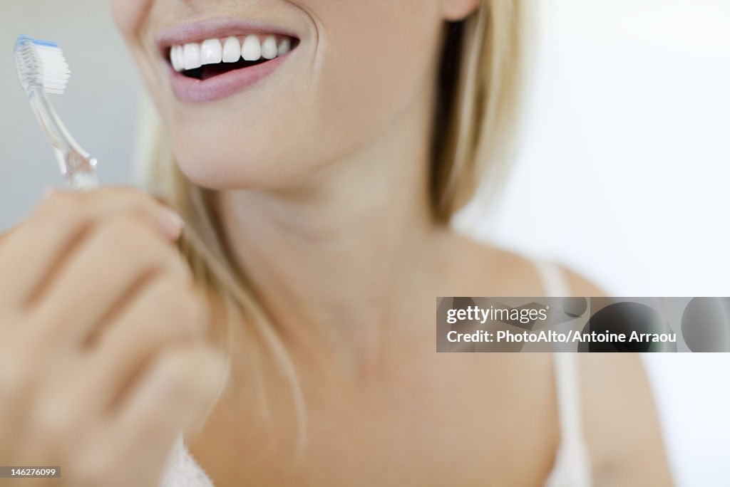 Smiling woman brushing teeth, cropped
