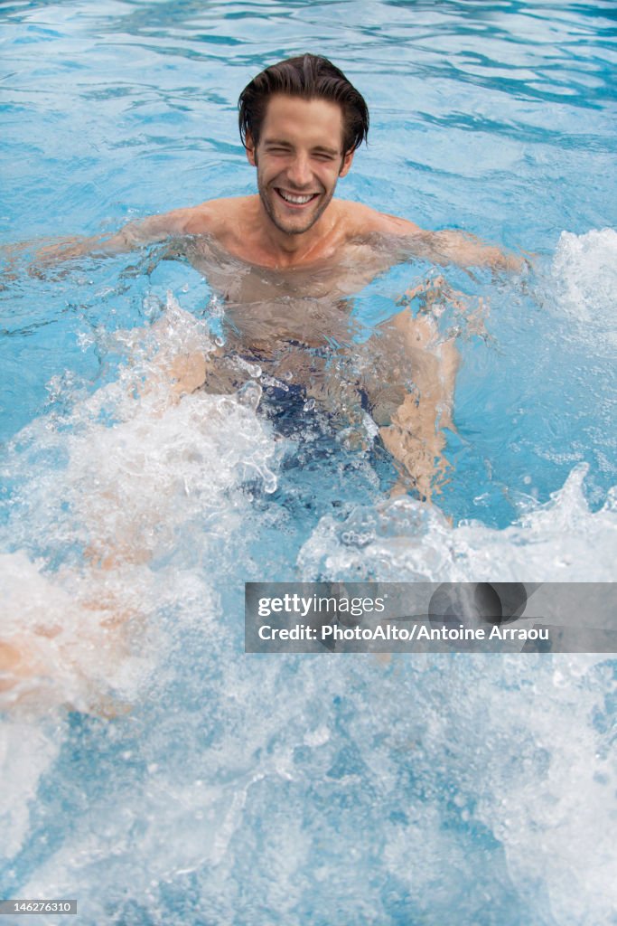 Young man kicking water in swimming pool