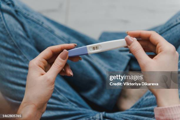 life events, family planning. high angle view of young woman sitting on the bed and holding a positive pregnancy test. - zwangerschapstest stockfoto's en -beelden