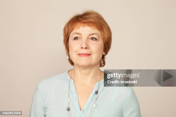 close-up studio portrait of a white active senior woman with red hair in a blue blouse on a beige background - red blouse stock pictures, royalty-free photos & images