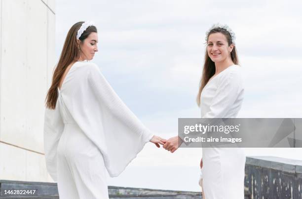 caucasian brides walking backwards and holding hands in a happy and smiling attitude. - lesbian beach wedding stock pictures, royalty-free photos & images