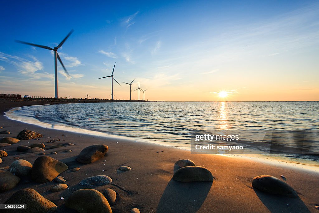 Sunset by beach with wind turbines
