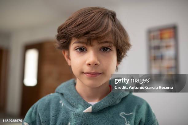 portrait of a 7 year old boy looking at camera with slightly long hair at home - boy brown hair stock pictures, royalty-free photos & images