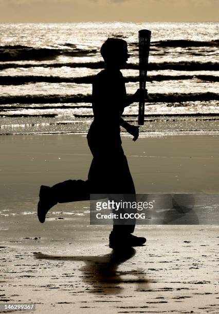 In this handout image provided by LOCOG, Torchbearer 002 Joseph Forrest runs along West Sands beach with the Olympic Torch during the London 2012...