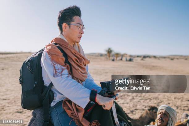 asian chinese male tourists getting up riding dromedary camel train crossing sahara desert morocco - digital single lens reflex camera stock pictures, royalty-free photos & images