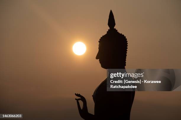 a silhouette buddha statue with the sun in the background - buddhismus stock-fotos und bilder