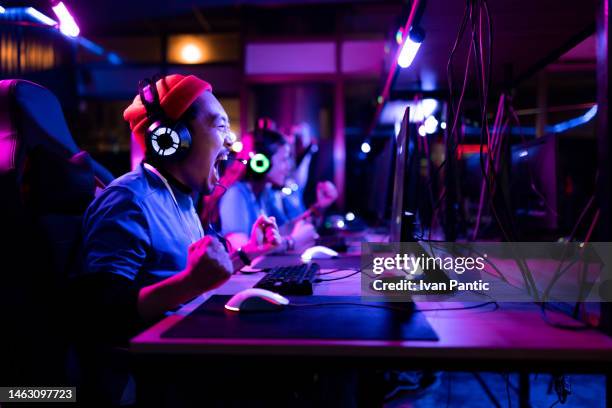 cheerful asian gamer celebrating his victory in esports video games at gaming club. - streamer stock pictures, royalty-free photos & images