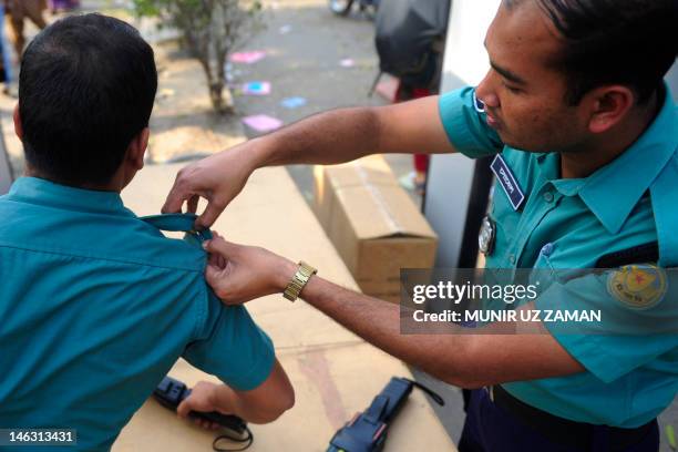 Bangladeshi law enforcement officer helps a colleague to fix his badge at the entrance point of a book fair in Dhaka on February 28, 2012. AFP...