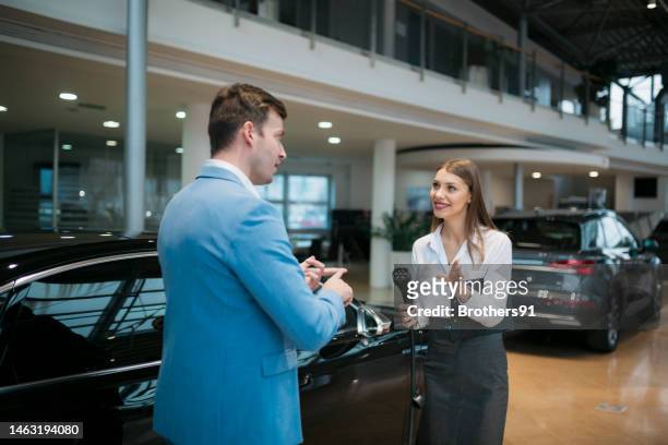 female sales manager selling electric car to a male customer at showroom - exclusive dealing stockfoto's en -beelden