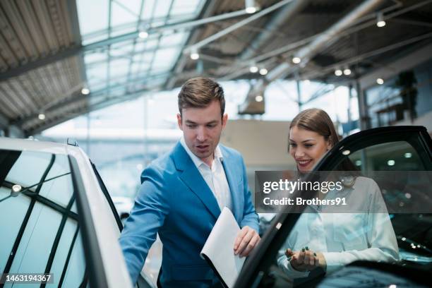 sales manager showing car to female customer in a car dealership - owner stand stockfoto's en -beelden