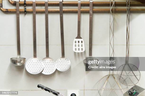 spoons and kitchen utensils hanging from a pipe on the wall of a restaurant in a front view. - pendurar imagens e fotografias de stock