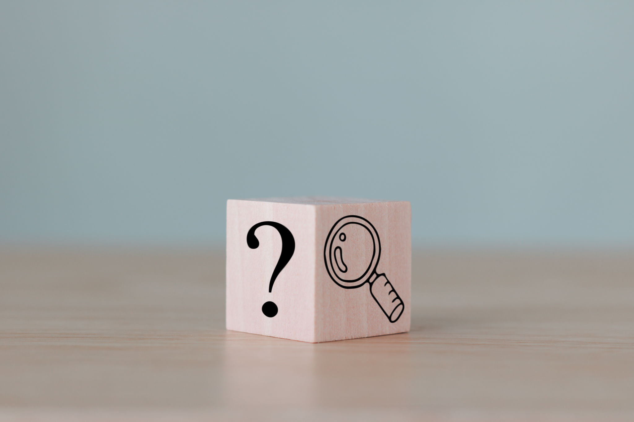 The wooden cube block with an illustration magnifying glass to analyze the question mark sign is isolated on the table. Problems and root cause analysis concept. Define problems to find solutions. The wooden cube block with an illustration magnifying glass to analyze the question mark sign is isolated on the table. Problems and root cause analysis concept. Define problems to find solutions.