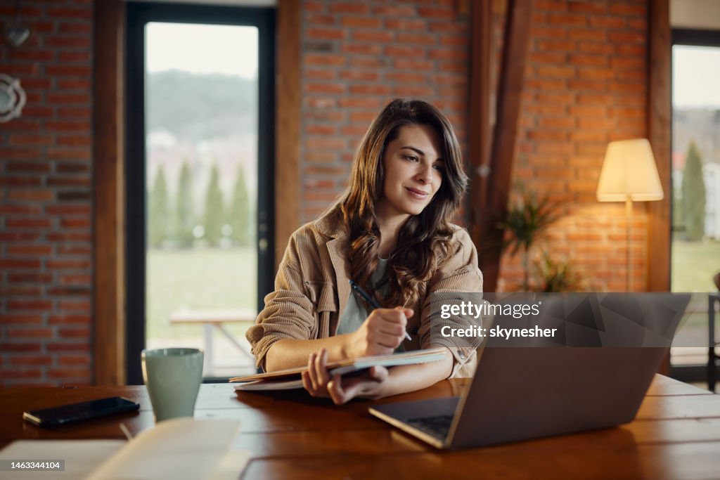 Creative woman taking notes while working on laptop at home office.