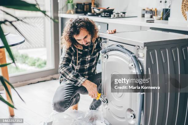 man in a kitchen repairing a washing machine. - buying washing machine stock pictures, royalty-free photos & images