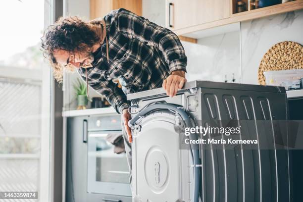 man in a kitchen repairing a washing machine. - plumbing products stock pictures, royalty-free photos & images