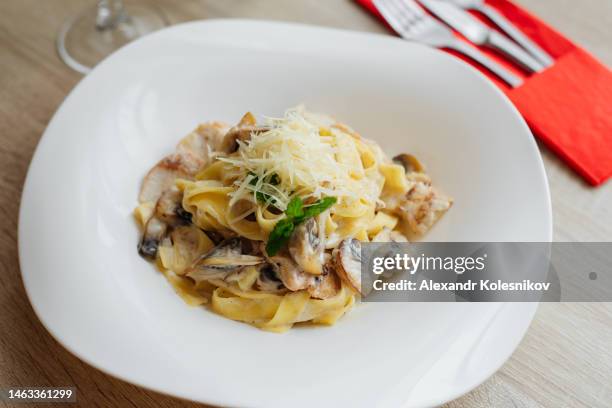 pasta fettuccine with mushrooms and fried chicken in creamy cheese sauce on a light wooden background - bechamelsoße stock-fotos und bilder