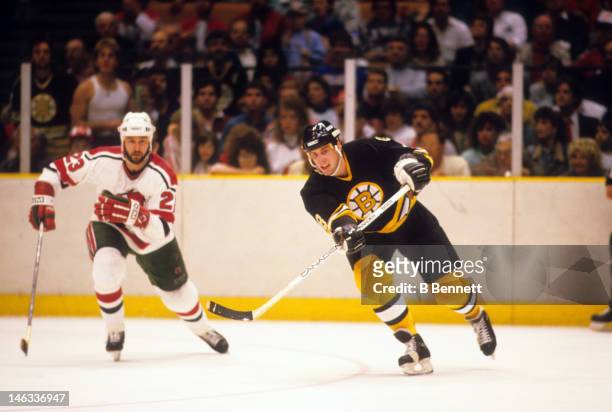 Cam Neely of the Boston Bruins passes the puck as he is pressured by Brude Driver of the New Jersey Devils on February 21, 1988 at the Brendan Byrne...