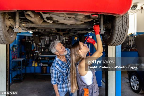 a couple of auto mechanics is fixing exhaust system under the lifted car. - car boken stock pictures, royalty-free photos & images