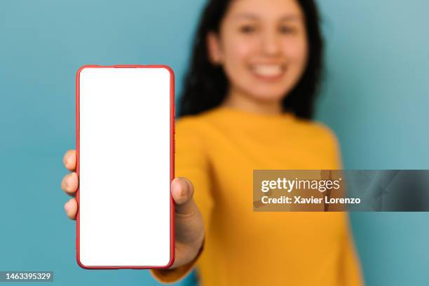 smiling young woman in yellow shirt showing white empty blank smartphone screen against blue background, close up. isolated mockup on mobile phone. - white shirt template stock pictures, royalty-free photos & images