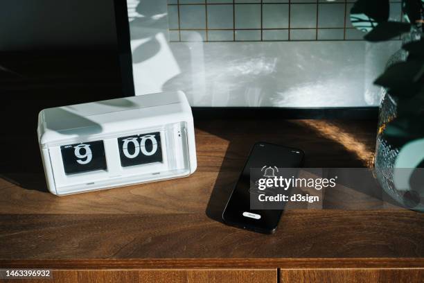 smartphone on wooden cabinet rings at nine o'clock, next to digital flip clock at home interior. sunbeam shining through the window on a fresh morning. a brand new day, fresh start, fresh energy, new opportunities. waking up early for a healthy lifestyle - alarm stockfoto's en -beelden