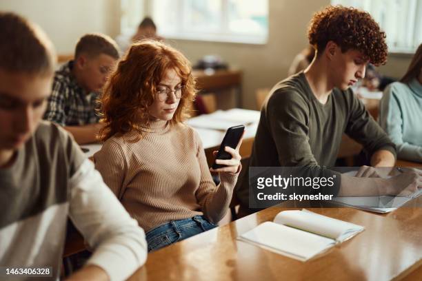 redhead female student using cell phone on a class at school. - university classroom stock pictures, royalty-free photos & images