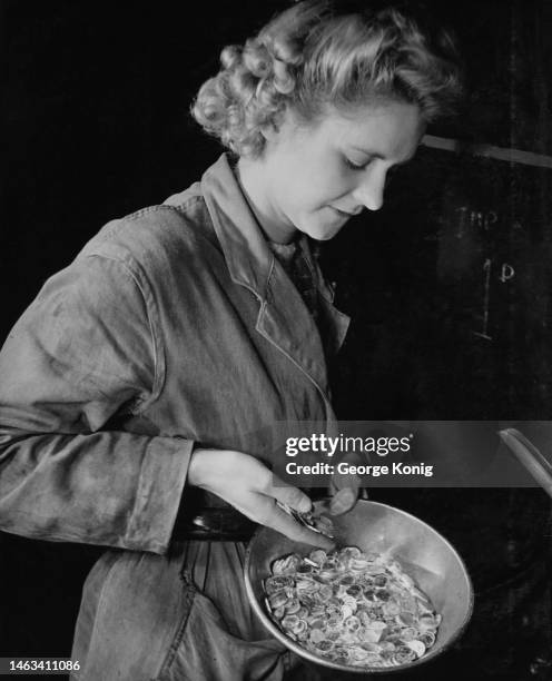 An coin press operator examines newly-struck imperial sixpences in the press room of the Royal Mint in London, England, circa 1945.