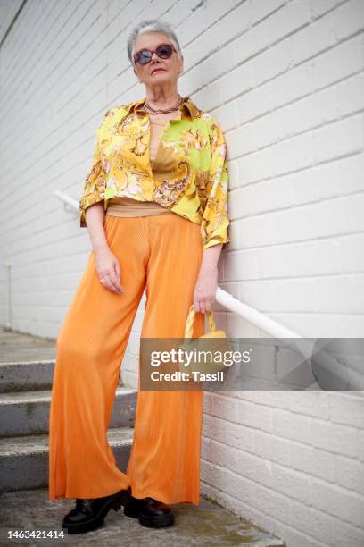 fashion, senior woman and modern style with attitude, confidence and proud, relax and leaning against a wall. stylish, elderly and lady empowered, fashionable and trendy clothing, cool and retired - luxury handbag stock pictures, royalty-free photos & images