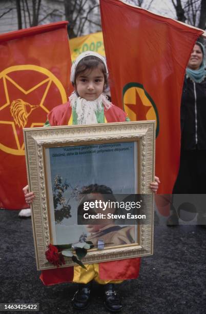 Young girl in traditional dress holds a framed portrait of PKK leader Abdullah Ocalan with a rose attached during a demonstration against his arrest...