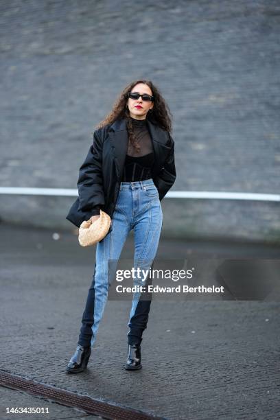 Guest wears black sunglasses, a black turtleneck transparent tulle t-shirt, a black velvet corset, a black nylon puffer jacket, a beige braided shiny...