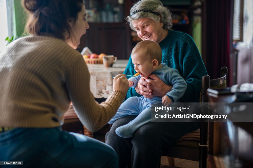 Mother and grandmother feeding little baby boy.