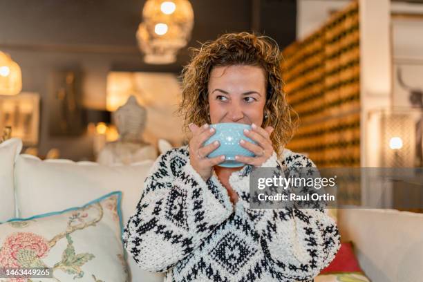 woman drinking soup from bowl sitting on the sofa at home - soup home foto e immagini stock