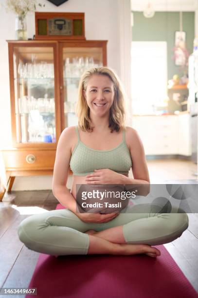 portrait, pregnant and woman on a floor for yoga, peace and zen, workout and happy in her home. pregnancy, face and hand on stomach for meditation, chakra and balance, relax and smile in living room - lotuspositie stockfoto's en -beelden
