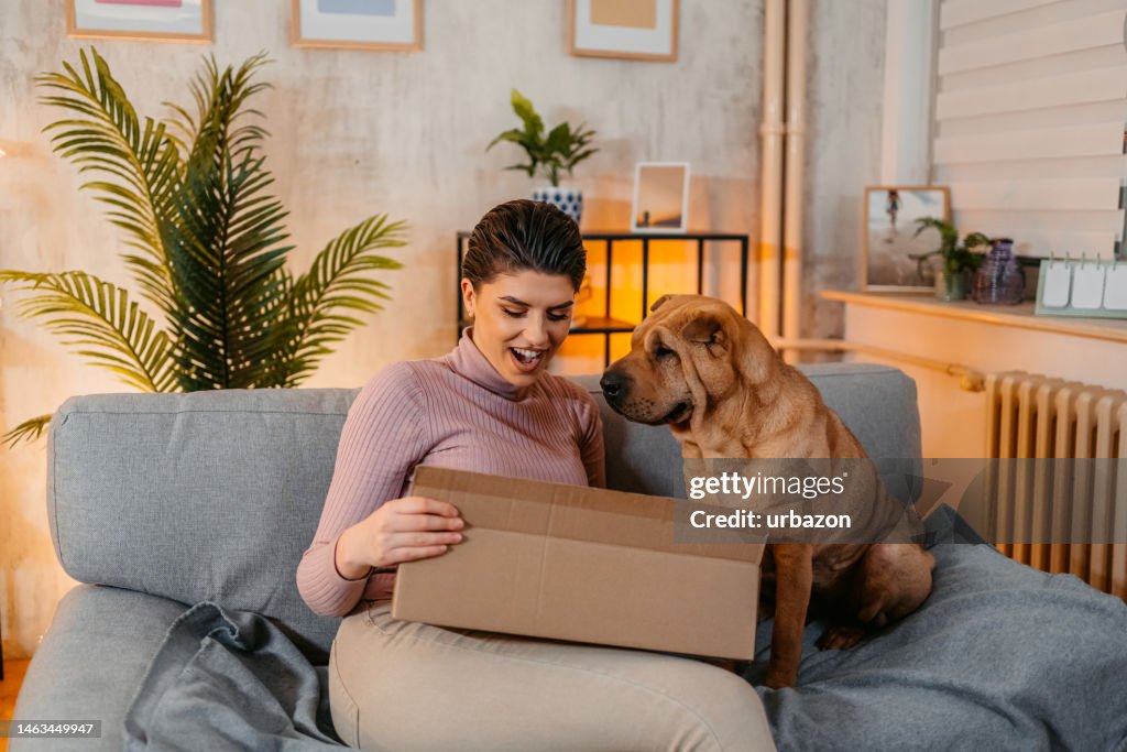 Young Woman With Her Dog Unpacking A Package She Ordered Online
