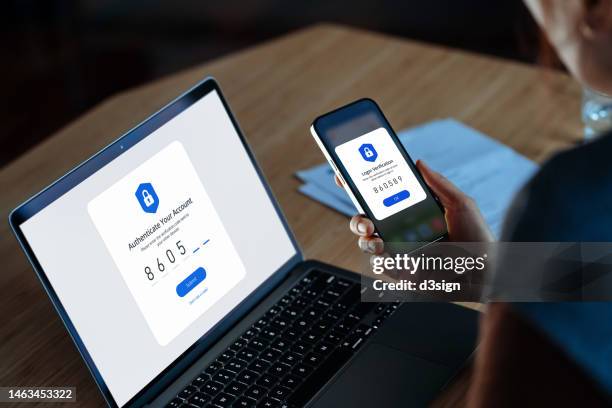 over the shoulder view of young woman using mobile device with two-factor authentication (2fa) security while logging in securely to her laptop. privacy protection, internet and mobile security - security_(finance) bildbanksfoton och bilder