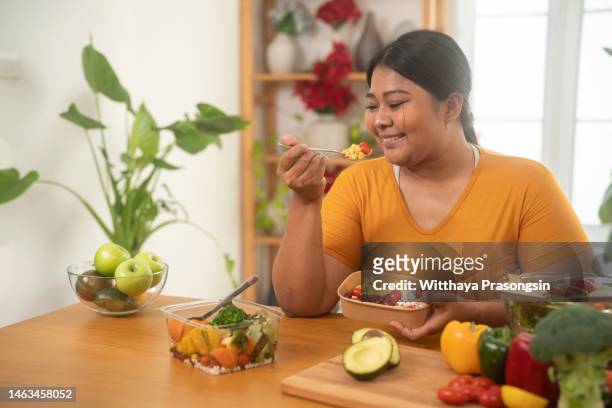 overweight woman eating healthy meal in kitchen - grasso nutrienti foto e immagini stock