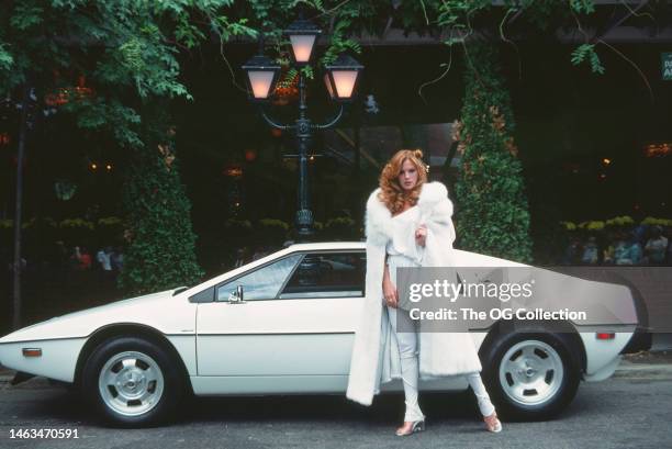 Portrait of American model and actress Victoria Lynn Johnson as she stands beside her Lotus Esprit sportscar, June 1977. The car was one of the...