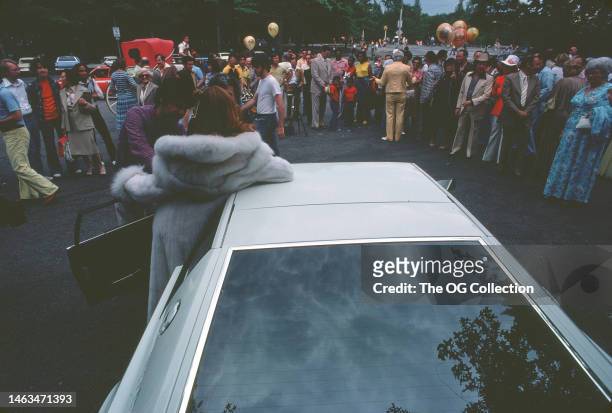 View, from behind, American model and actress Victoria Lynn Johnson in the open door of her Lotus Esprit sportscar, June 1977. Spectators, some with...