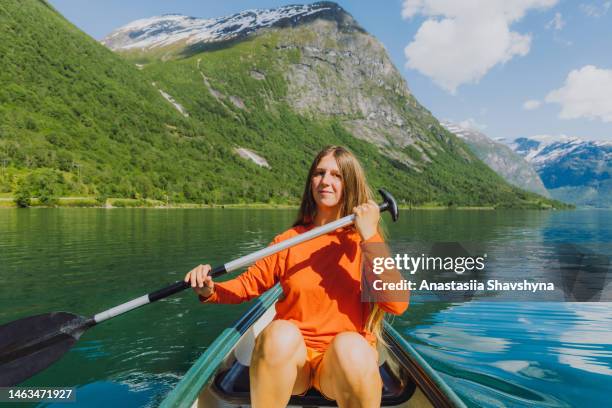 vorderansicht einer lächelnden frau im orangefarbenen kanu im malerischen lovatnet-see in norwegen - skandinavischer abstammung stock-fotos und bilder