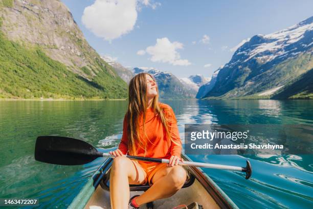 front view of smiling woman in orange canoeing in scenic lovatnet lake in norway - summer norway people stock pictures, royalty-free photos & images