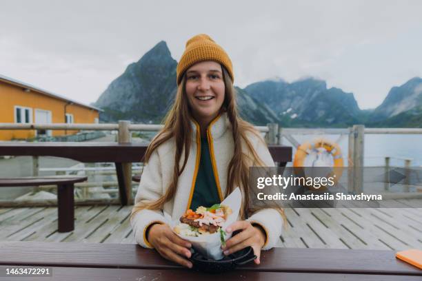 a woman in yellow hat enjoying delicious seafood meal with fjord view on lofoten islands - norwegian culture stockfoto's en -beelden