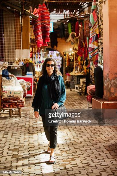 wide shot of smiling mature woman walking through souks in marrakech - maroc business stock-fotos und bilder