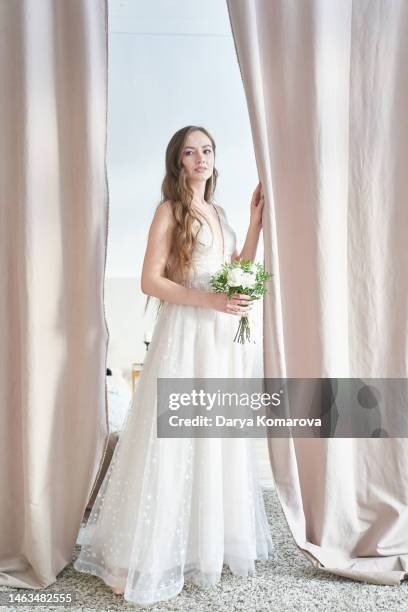 a beautiful young bride in a wedding dress and flowers walks through a room with a beautiful interior with curtains dividing the room. a woman in a full-length long dress. a lifestyle with a copy space. - fabulous full lengths foto e immagini stock