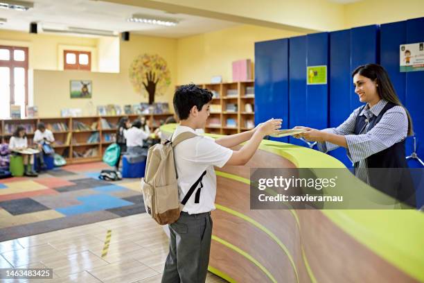 studente che controlla il libro dalla biblioteca scolastica - bibliotecario foto e immagini stock