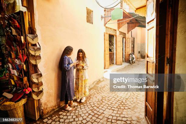 wide shot of sisters looking at smart phones in the souks of marrakech - moroccan girls stock pictures, royalty-free photos & images