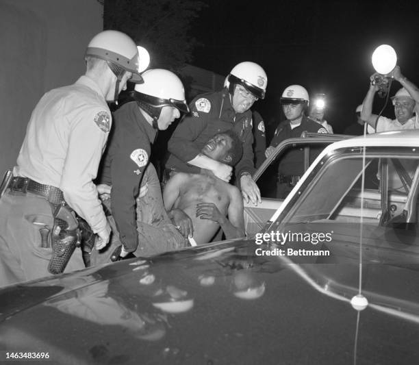 Police officers force rioters into police cars during the second night of rioting in the Watts district of Los Angeles.