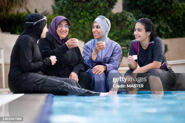 joyful muslim women drinking coffee at pool - hiyab fotografías e imágenes de stock