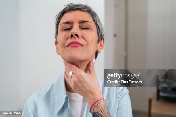 mujer tocando su dolor de garganta, mientras hace una mueca debido al dolor - throat photos fotografías e imágenes de stock